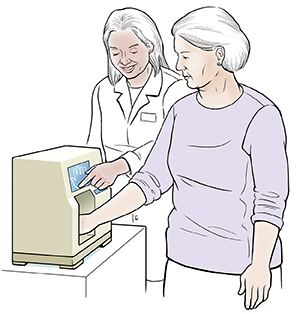 Healthcare provider giving woman bone density test. Woman's hand is in small machine.