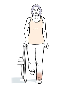 Woman standing, holding on to chair doing balance exercise on one leg.