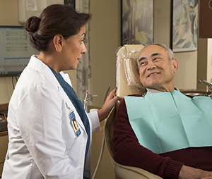Proveedor de atención médica, hablándole a un paciente que está sentado en un sillón de examen odontológico.