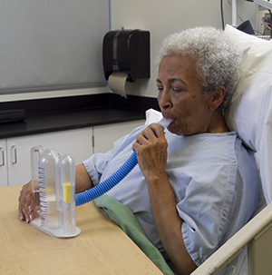 Mujer con una bata de hospital, usando un espirómetro.