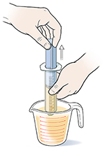 Primer plano de manos extrayendo alimento líquido con una jeringa de un vaso de medición.