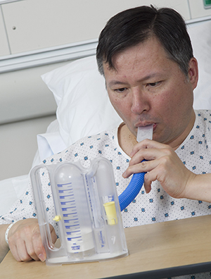 Hombre usando un espirómetro de incentivo en una cama de hospital.