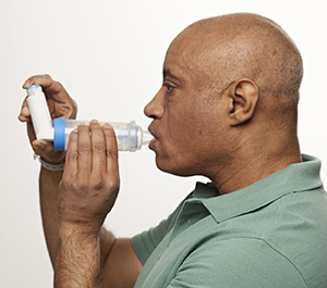 Hombre que usa un inhalador de dosis medida con un espaciador.